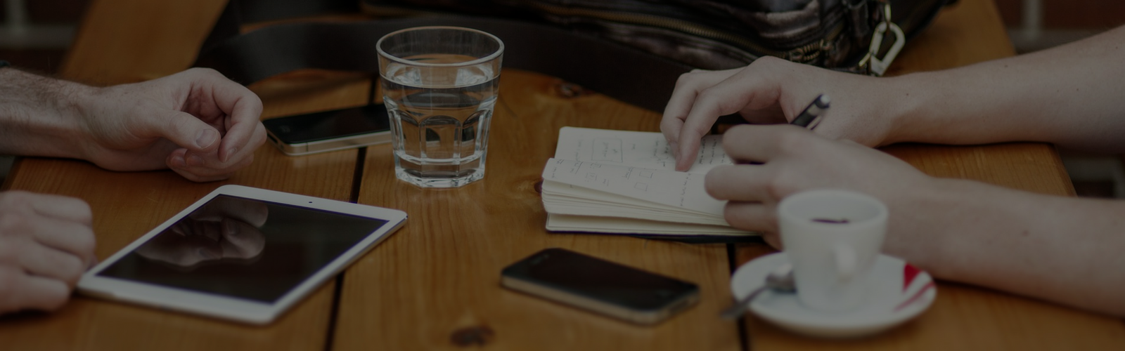 Tablet and two smart phones on a table with someone taking notes