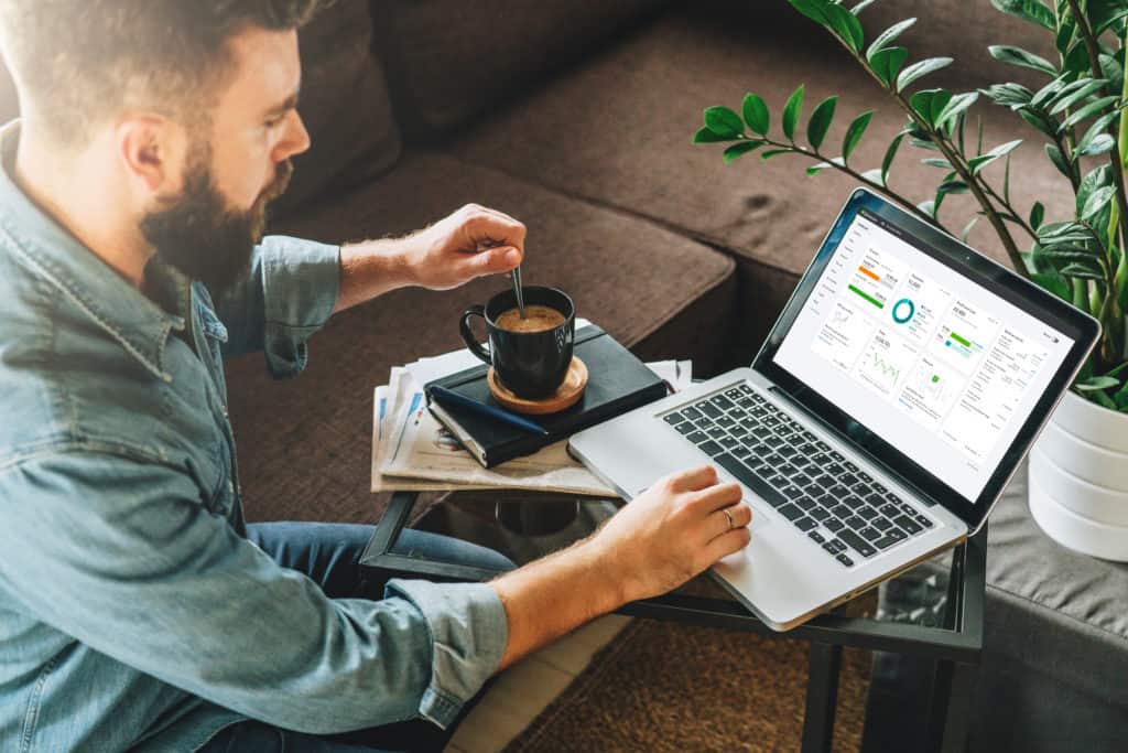 Man stirring coffee looking at a laptop