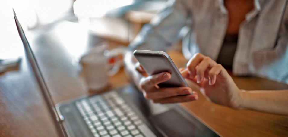 Someone holding a smartphone over a laptop